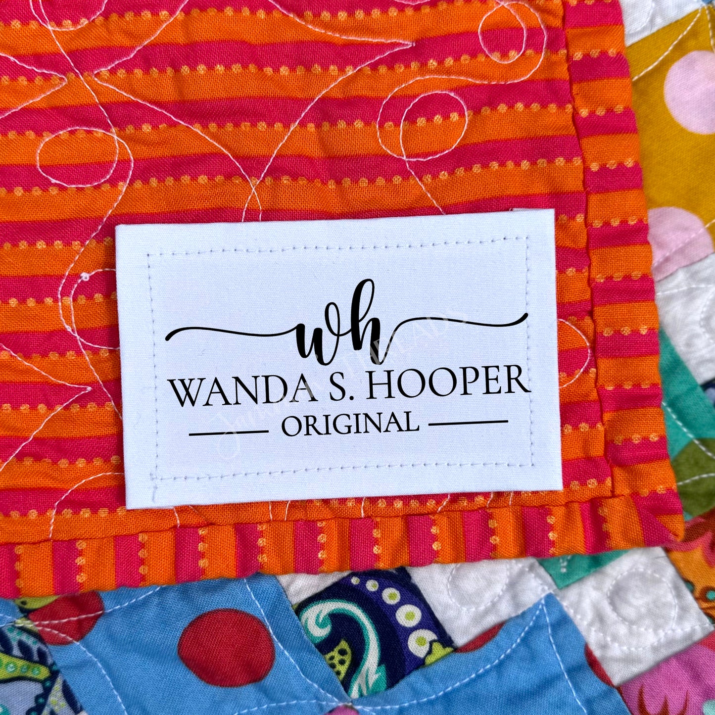 Personalized quilt label with maker monogram and name sewn onto a colorful quilt binding, logo-style label for handmade quilts.