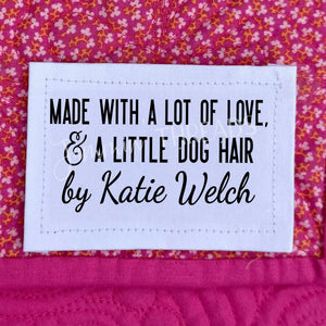 Personalized quilt label reading “Made with a lot of love and a little dog hair” with maker name sewn onto a quilt.