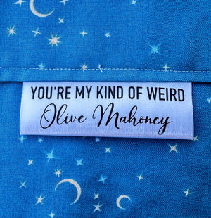 Personalized “You’re My Kind of Weird” satin quilt tag with maker name sewn into blue star fabric quilt binding, custom sewing label by Jammin’ Threads