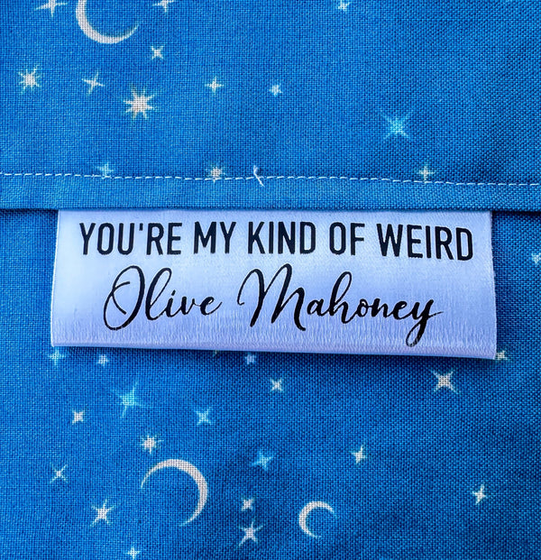 Personalized “You’re My Kind of Weird” satin quilt tag with maker name sewn into blue star fabric quilt binding, custom sewing label by Jammin’ Threads