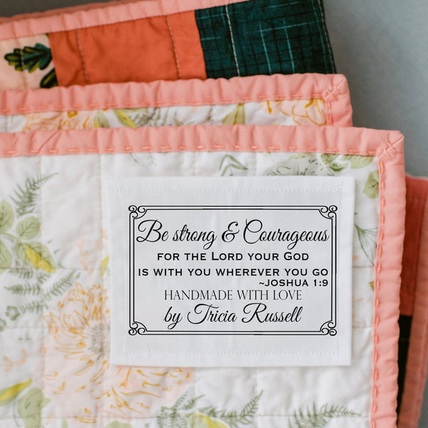 Personalized quilt label with Bible verse Joshua 1:9 reading “Be strong and courageous for the Lord your God is with you wherever you go” sewn onto a quilt.