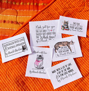 Assortment sheet of six funny sarcastic cat quilt labels with humorous sayings sewn onto a quilt.